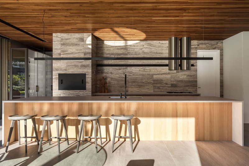 Kitchen island with timber base illuminated by afternoon light beneath a striated travertine feature wall