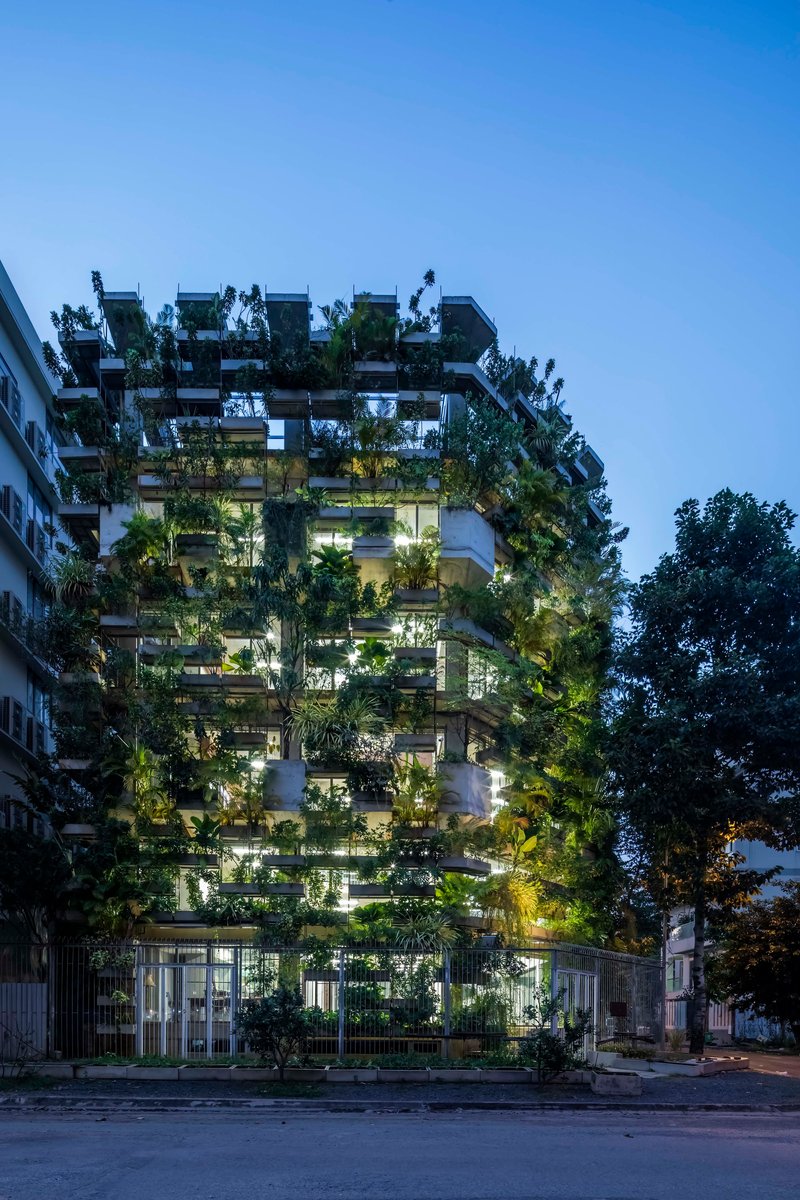 Street facade of the tower densely planted with trees on every balcony at twilight