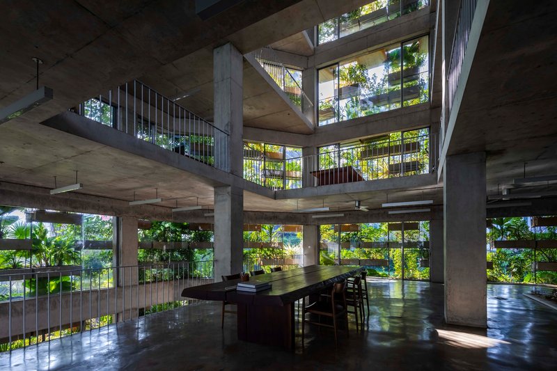 Interior atrium with concrete columns and cantilevered floors framing planted balconies in dappled sunlight