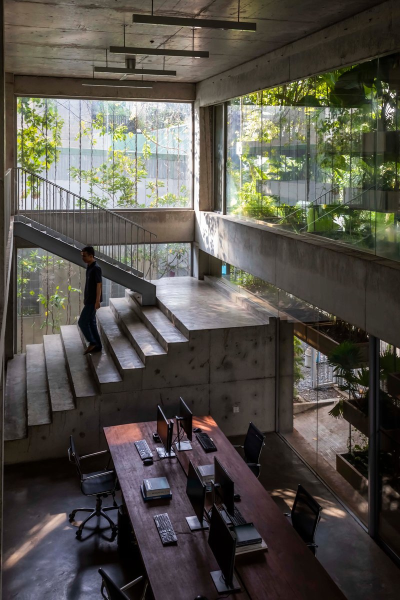Concrete staircase ascending through multi-level workspace with person walking and vegetation outside windows
