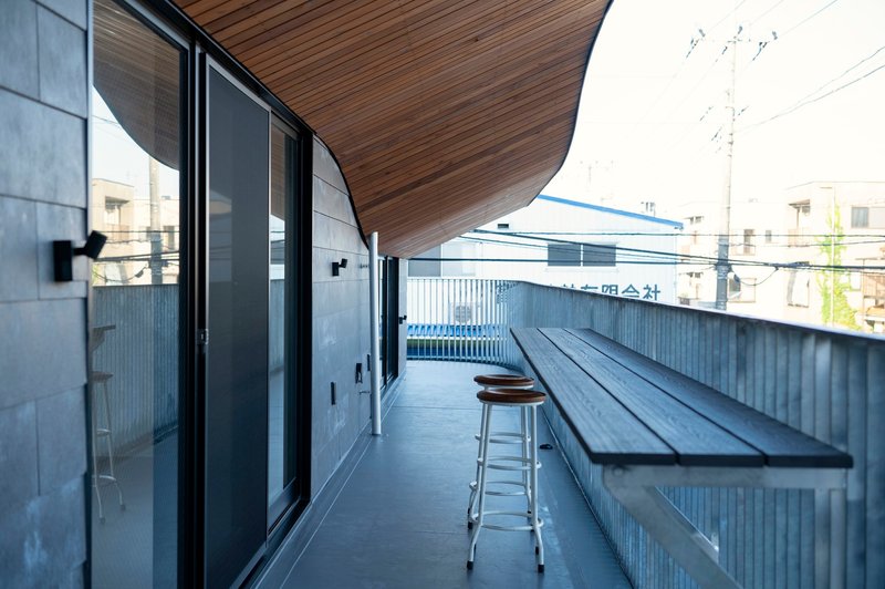 Narrow terrace with corrugated metal wall, black bench, and timber soffit above glass doors