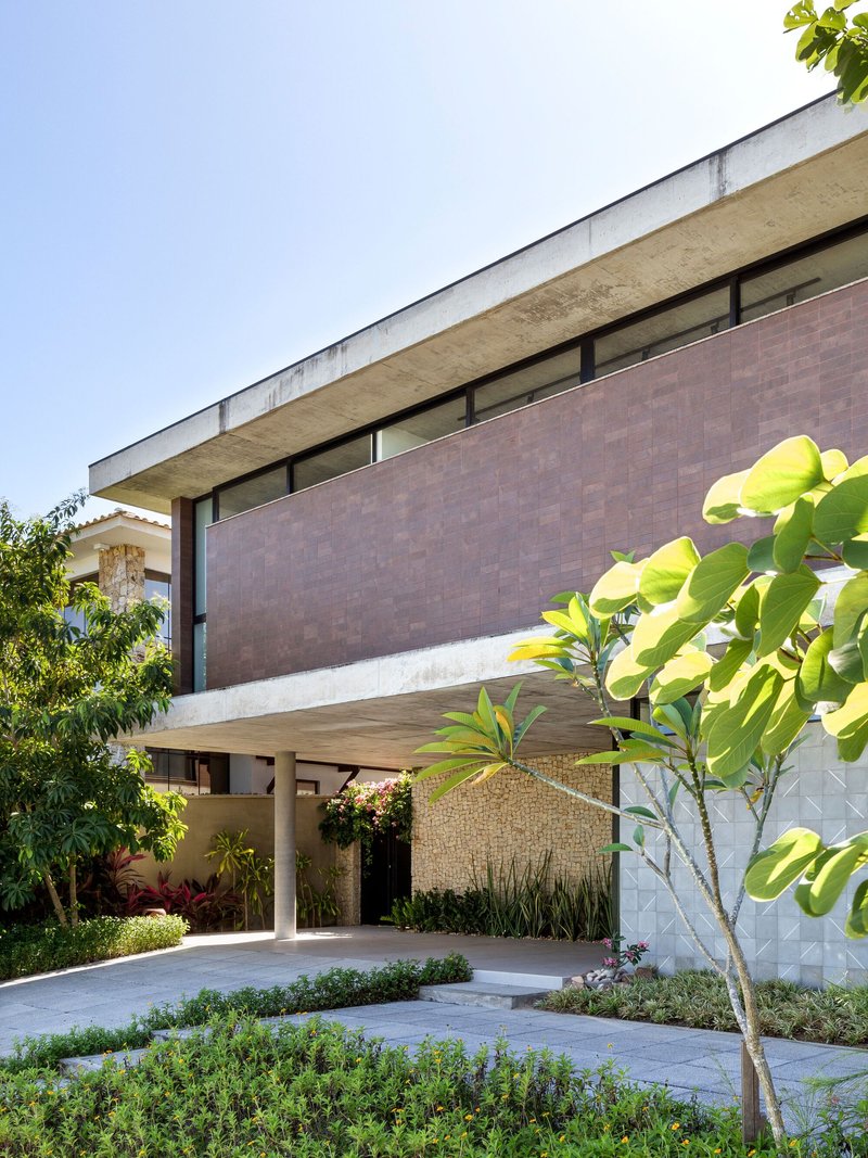 Cantilevered concrete slab shading the paved forecourt with planted beds and geometric textured wall below