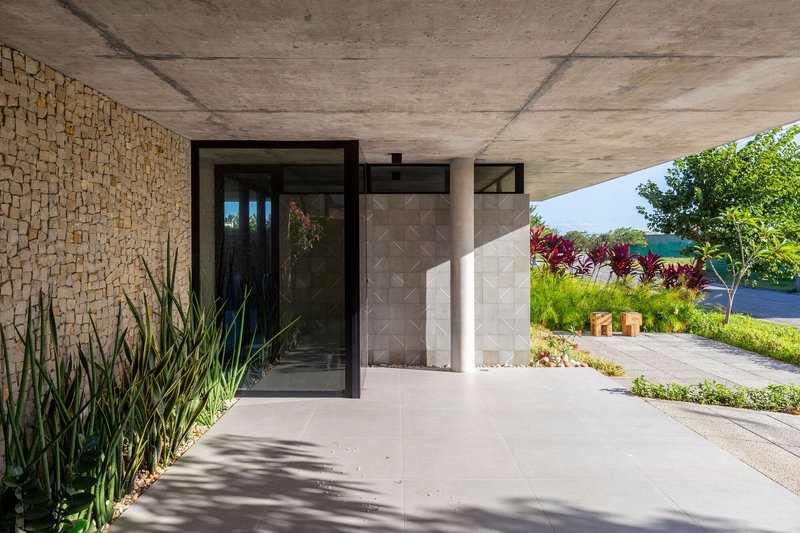 Entry path with patterned concrete wall and circular column beneath exposed concrete soffit with ornamental grasses