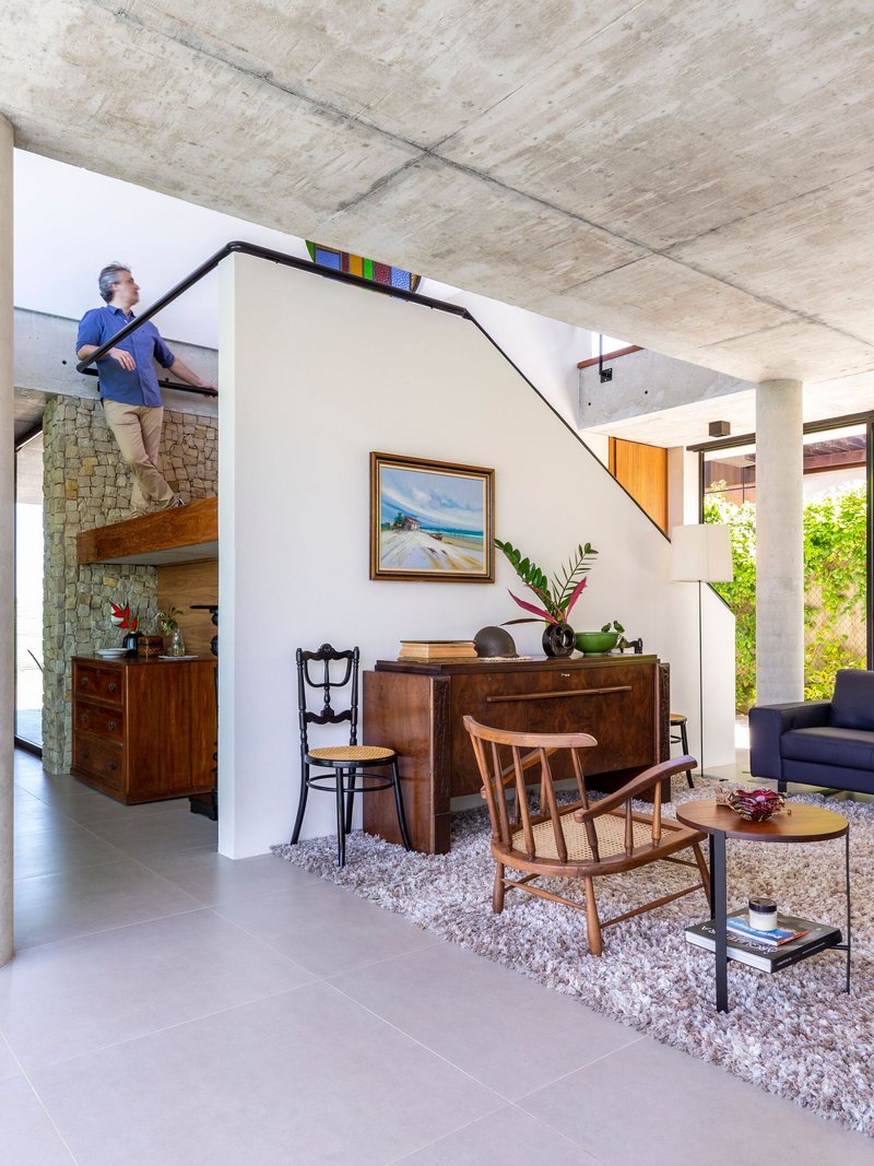 Living room with angled stair volume and exposed concrete ceiling while person ascends upper landing
