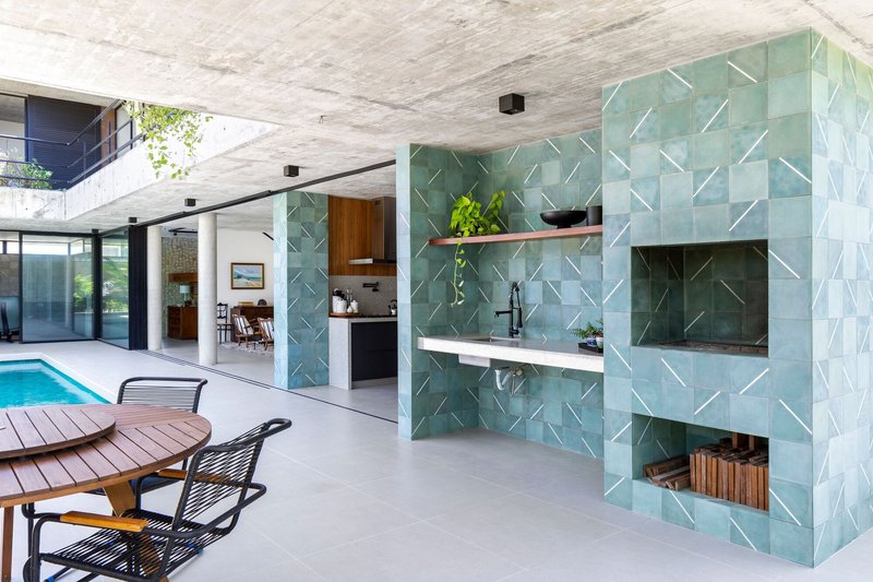 Covered patio with chevron-patterned turquoise tile kitchen wall and exposed concrete ceiling overlooking the pool