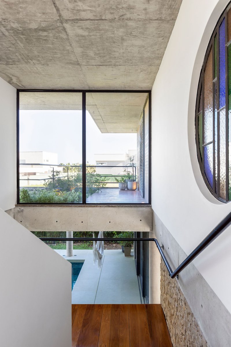 Double-height void with concrete beam, glazed balcony doors, and circular stained glass window beside the stair