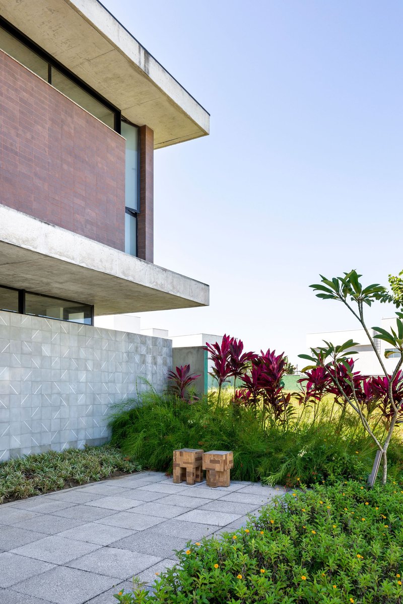 Concrete cantilever terrace above a geometric patterned wall with lush plantings and paving below