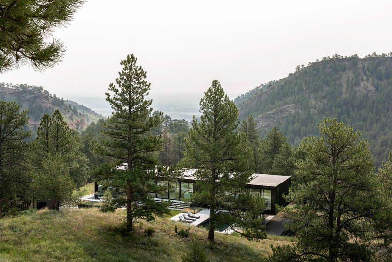 Hillside view of the residence nestled among pine trees with mountain ridges visible in the distance