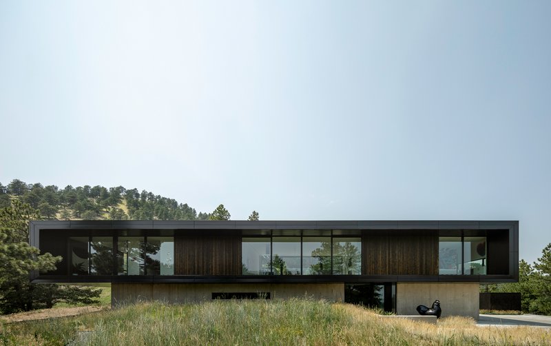 Long view of the dark timber and glass upper volume cantilevers over a concrete base in dry grassland