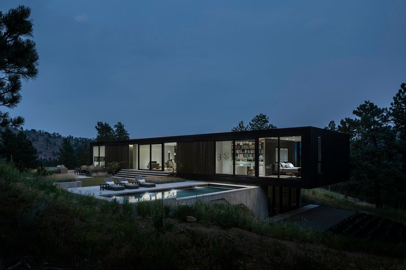 Black cladded residence with glazed openings above a concrete plinth and reflecting pool at twilight
