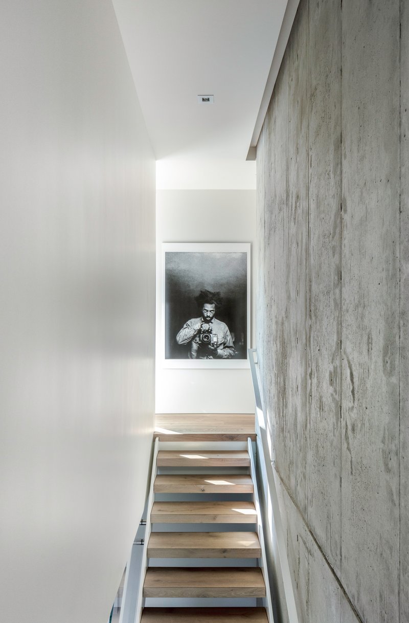 Staircase with floating timber treads alongside a board-formed concrete wall and framed photograph