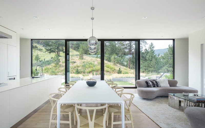 Open plan living and dining space with full-height glazing framing views of the hillside landscape
