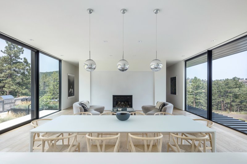White dining table with wishbone chairs beneath three globe pendant lights and symmetrical corner windows