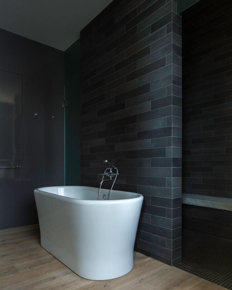 White freestanding bathtub against a dark brick tile wall in a dimly lit bathroom