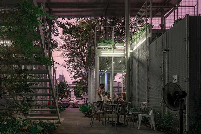 Covered ground-floor terrace with dining furniture surrounded by planted trees at twilight