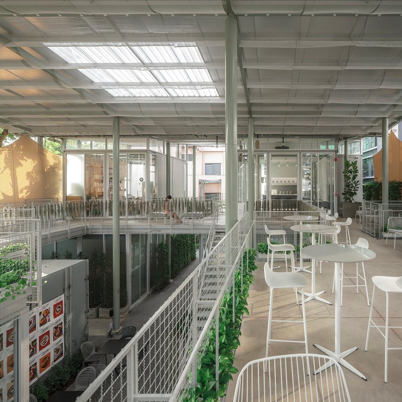 Interior terrace with white furniture and mesh railings overlooking planted voids under the translucent ceiling grid