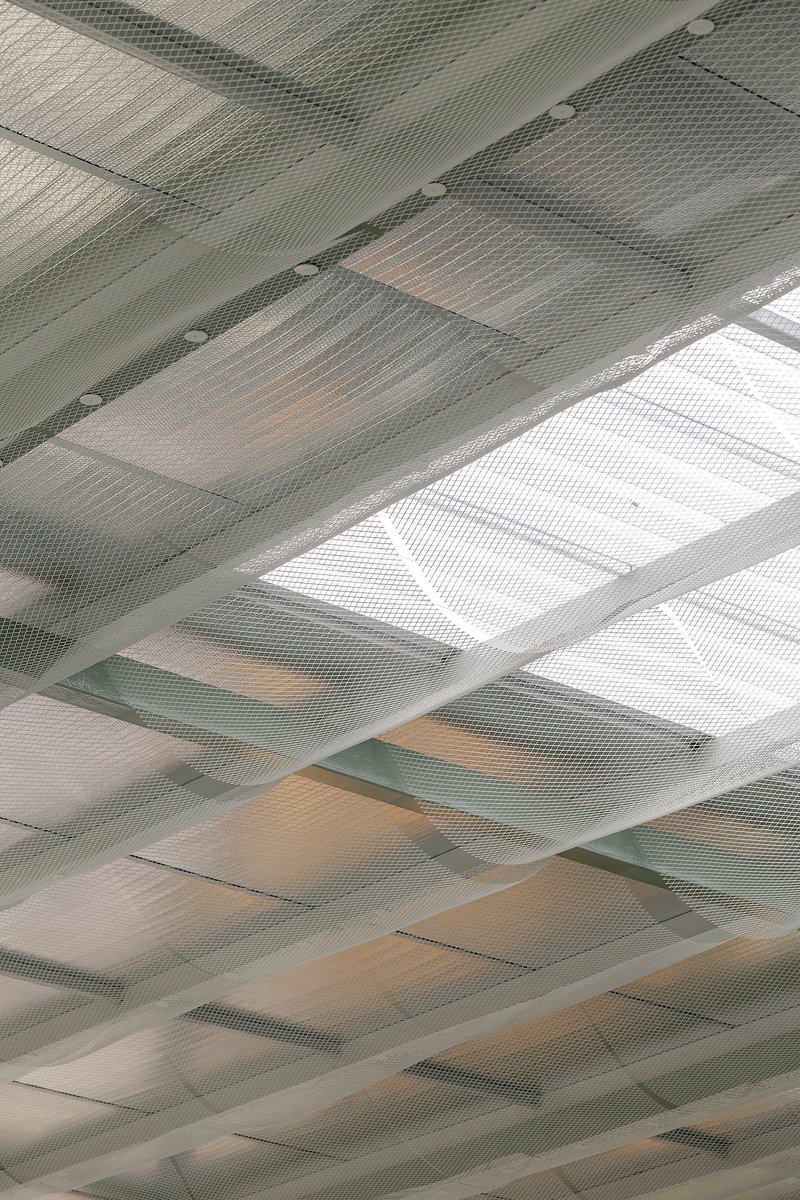 Perforated metal ceiling panels with integrated skylights casting geometric shadows across the surface