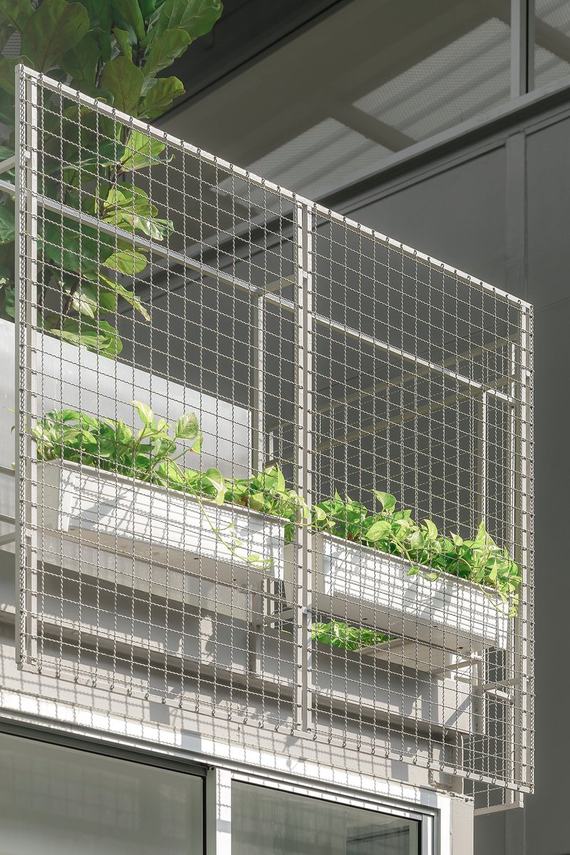Wire mesh facade screen with integrated planter boxes holding foliage in bright daylight