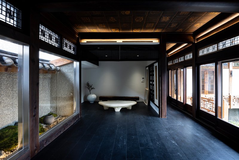 Interior corridor with dark timber frame and latticed transom windows overlooking a pebble courtyard