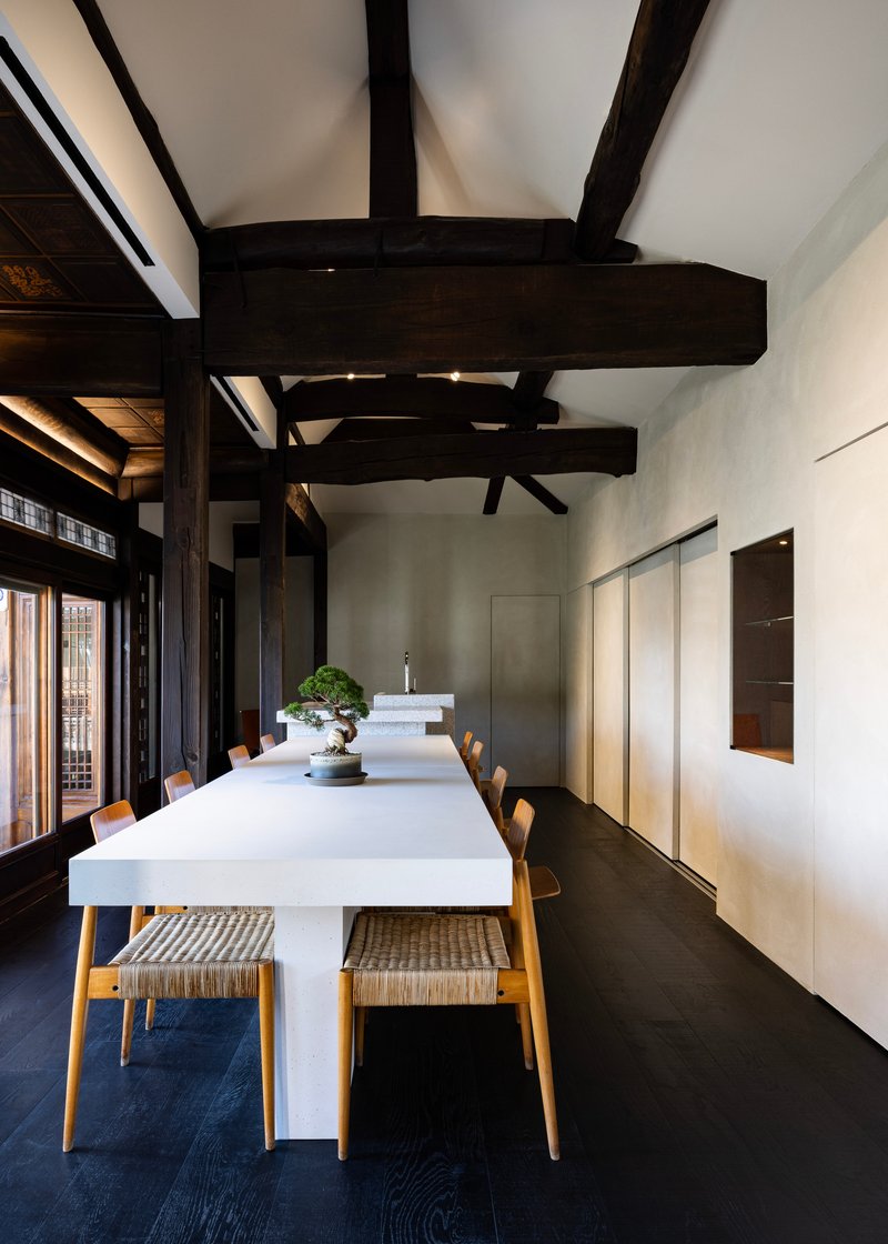 Dining room with exposed dark timber beams above a white table and wooden chairs on dark flooring