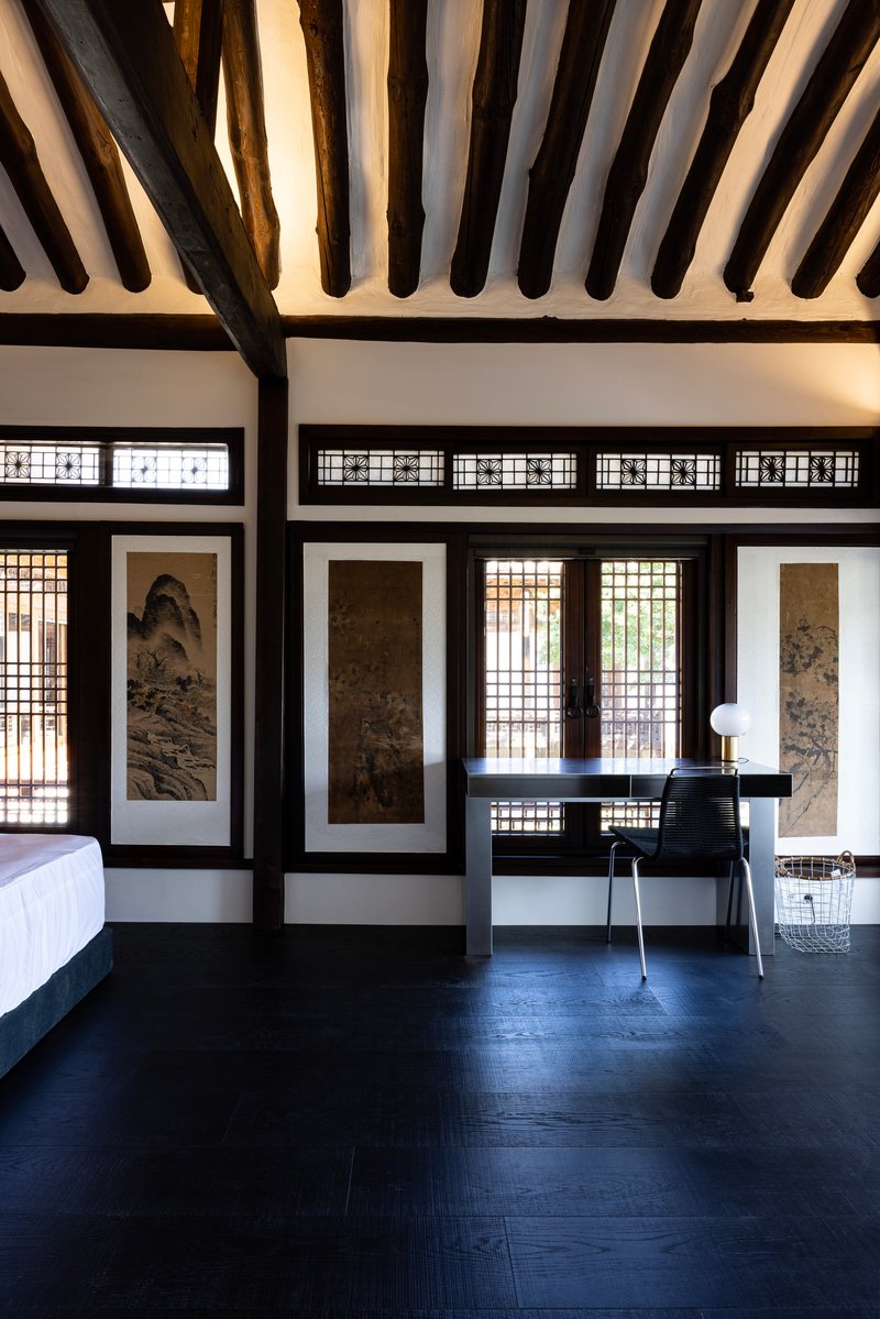 Room with exposed timber ceiling beams, latticed screens, framed scroll paintings, and dark wooden flooring