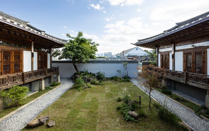 Central courtyard garden with gravel paths between two timber-framed pavilions under a cloudy sky