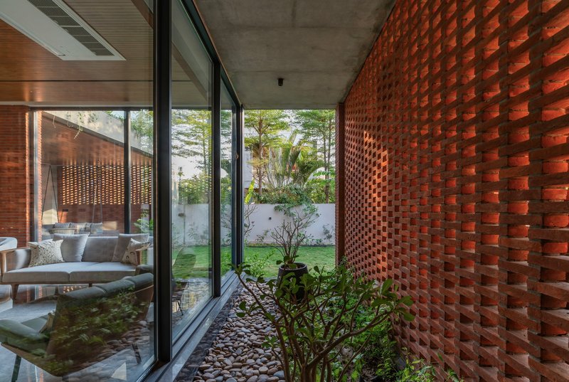 Covered passage with perforated red brick wall alongside a planted courtyard with shrubs and pebbles