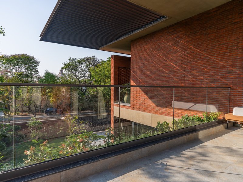 Upper terrace with glass balustrade overlooking a planted courtyard with red brick volumes beyond