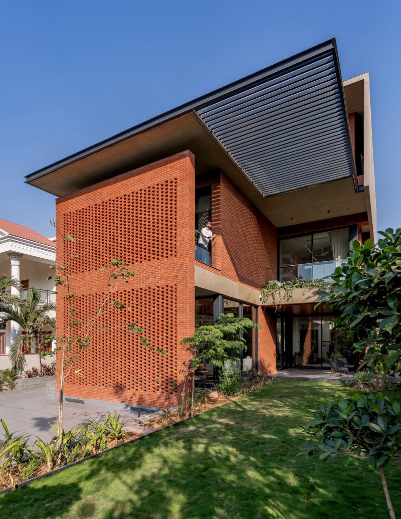 Garden view of perforated red brick facade and cantilevered metal roof under clear blue sky