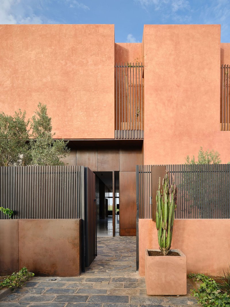 Entry courtyard with terracotta walls, timber screens, and stone paving under afternoon sunlight