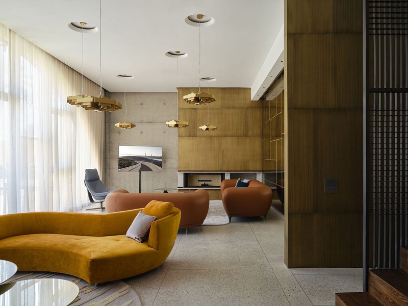 Seating area with exposed concrete wall and timber cabinetry under a double-height volume