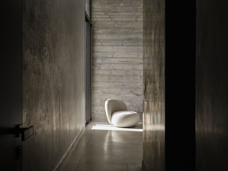 Narrow corridor with board-formed concrete walls and a single chair in sunlight