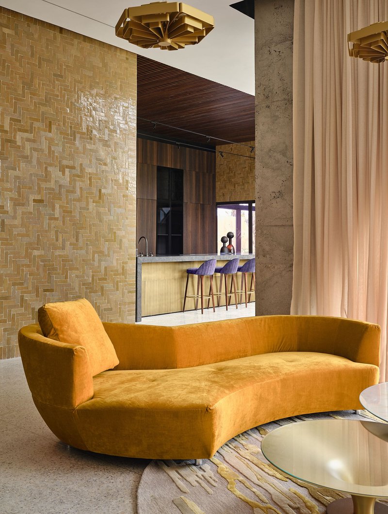 Living area with curved sofa facing basketweave tile wall and bar seating beneath ribbed timber ceiling