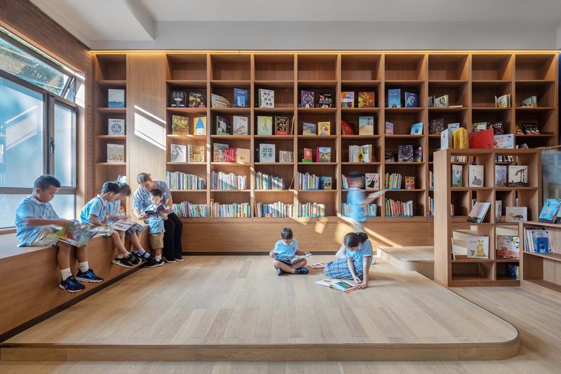 Library with floor-to-ceiling timber bookshelves and stepped seating where children sit reading in morning light