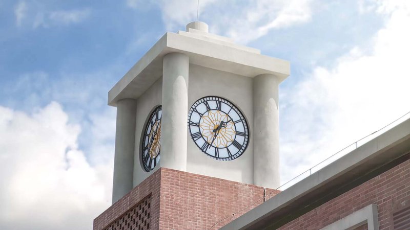 Clock tower with white rendered upper section and red brick base under cloudy sky