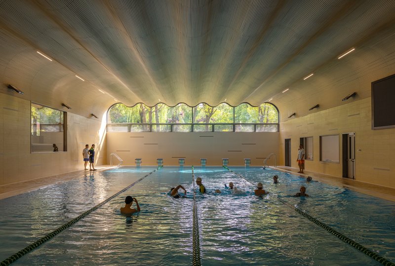Indoor swimming pool with arched clerestory windows and timber ceiling beams illuminated by natural light