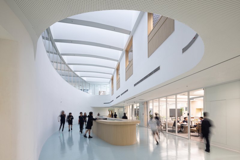 Oval skylight above a curved reception desk with people moving through the daylit lobby space
