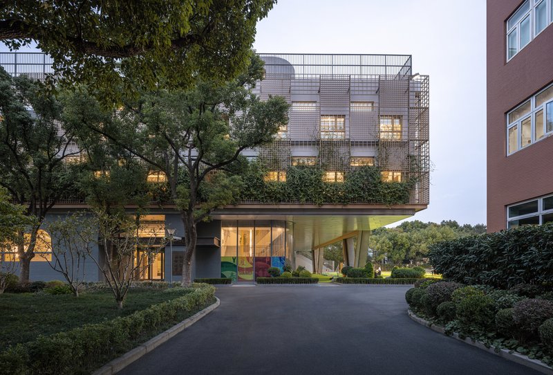 Elevated building with perforated metal facade and underlit cantilevered volume at dusk