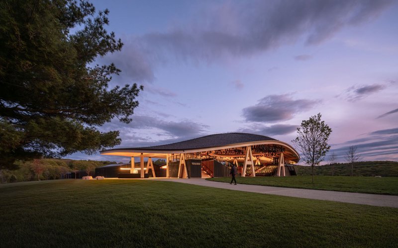 Ground level view showing timber A-frame columns supporting the sweeping roof at twilight