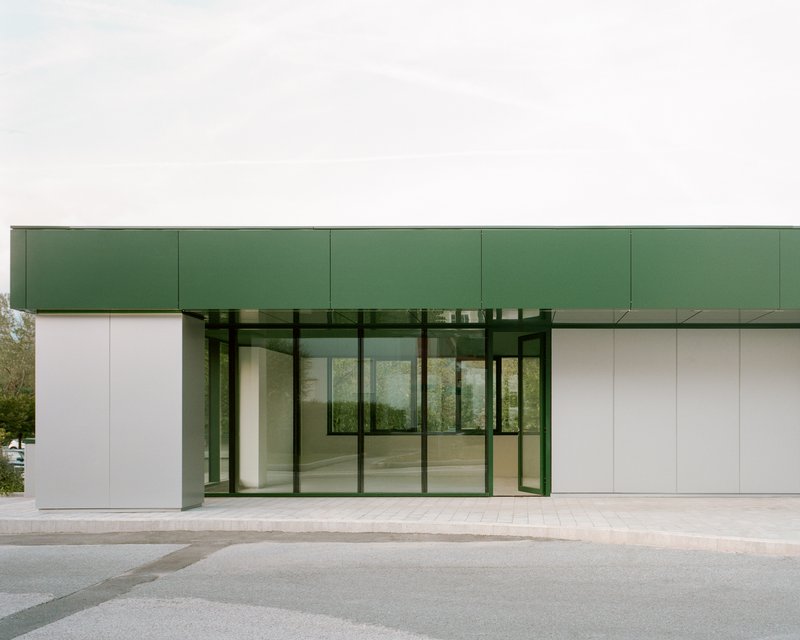 Recessed glass entry portal framed by white panels and green metal canopy under overcast sky