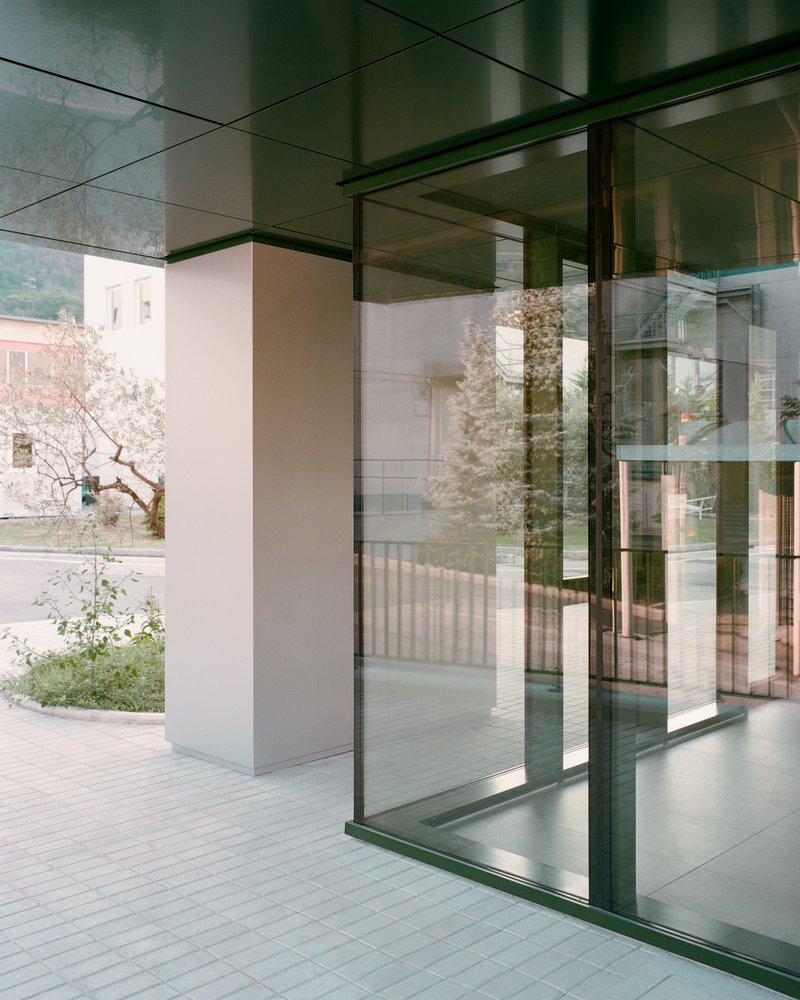View through glass facade showing layered reflections of courtyard trees and adjacent building volumes