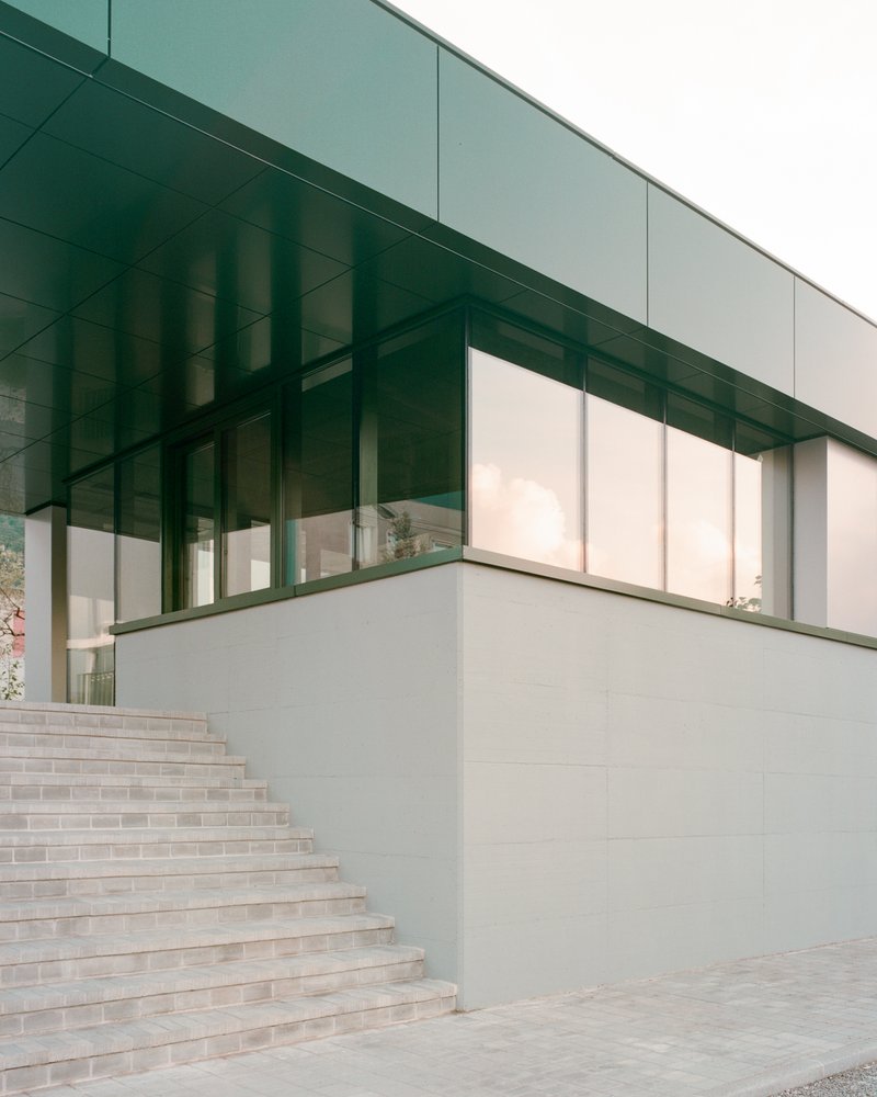 Exterior staircase ascending alongside corner glass volume with green metal soffit above