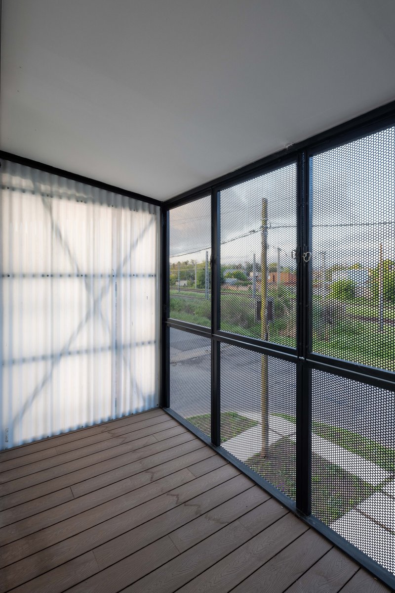 Balcony with timber decking enclosed by black-framed perforated mesh screens overlooking a suburban street