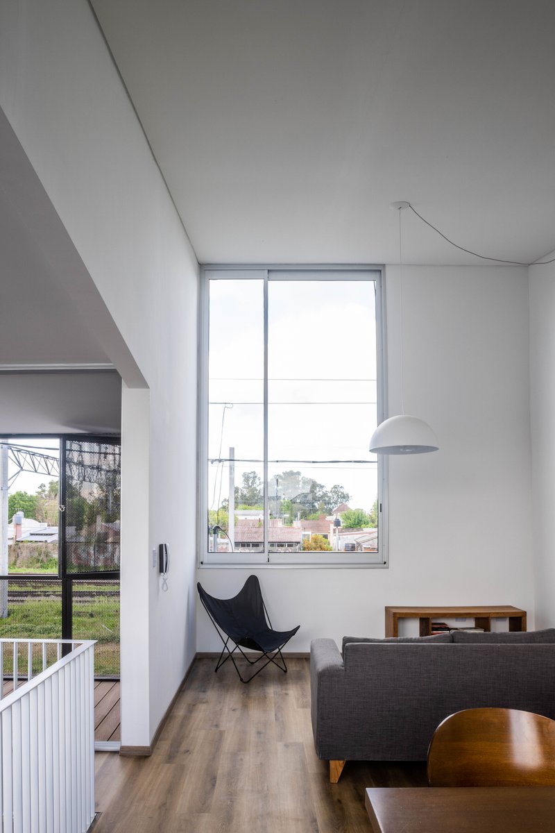Double-height living area with sloped ceiling and tall window framing view of suburban rooftops