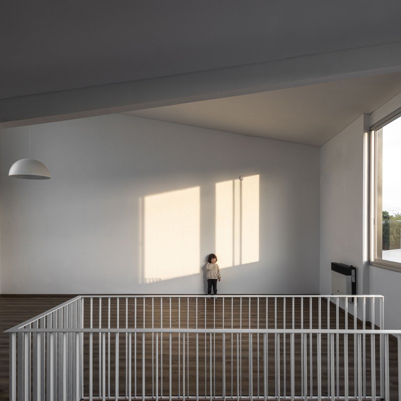 Upper floor room with white walls and slatted railing where child stands in afternoon sunlight