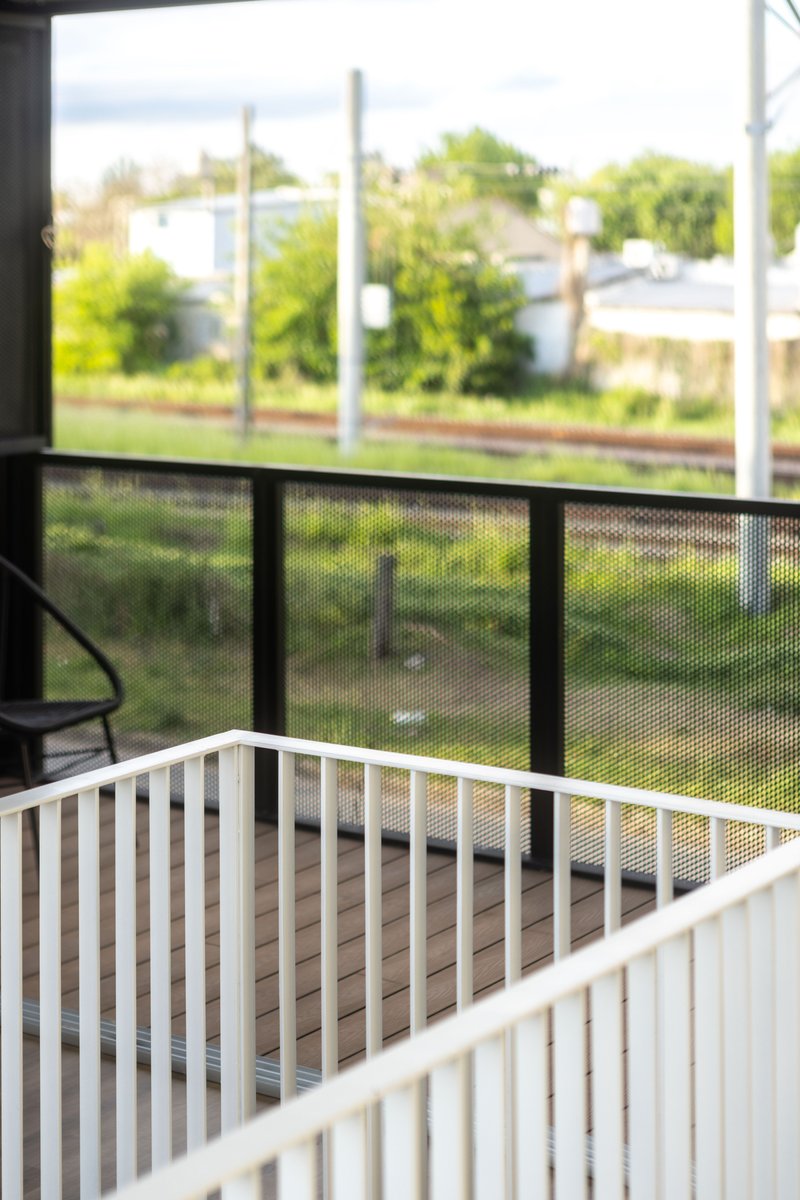 Interior view from the balcony with metal mesh railing overlooking the railway line and vegetation