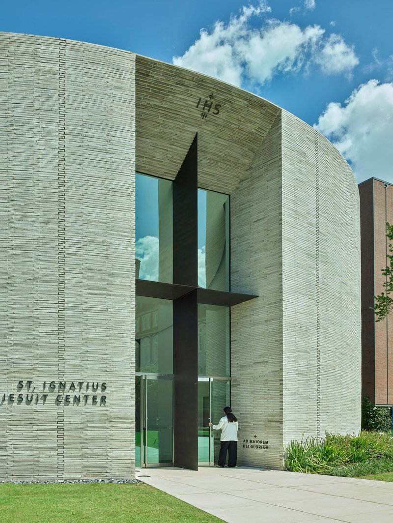 Glazed cross cutting through the layered grey brick entrance facade on a sunny day