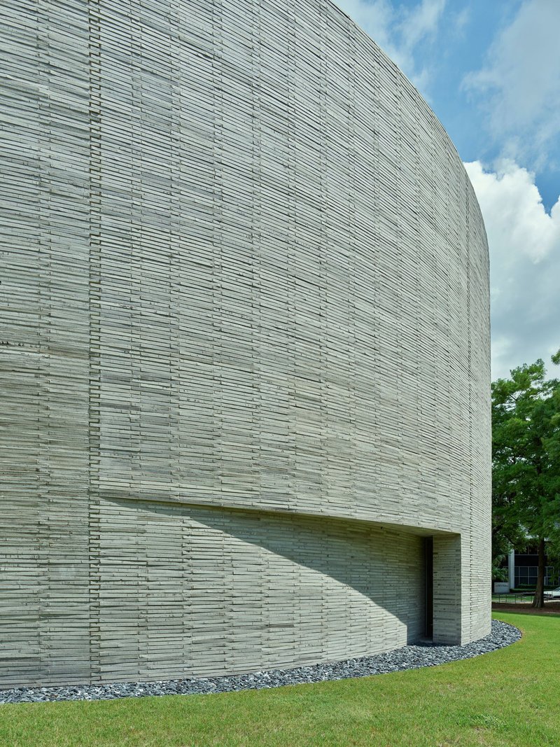 Close-up of the curved brick wall showing recessed entry slot beneath white clouds