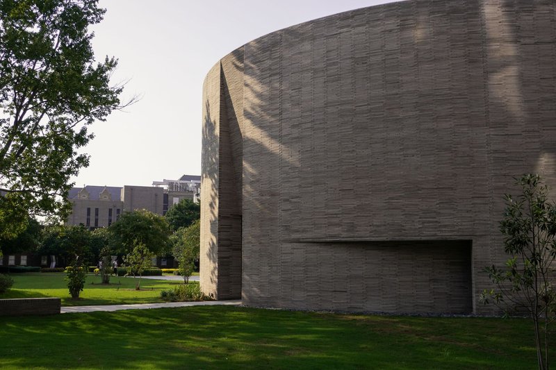 Curved brick chapel volume rising above a green lawn with trees casting afternoon shadows