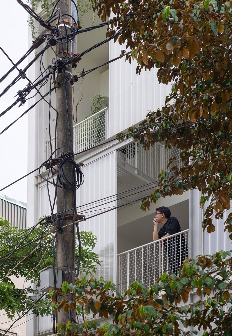 Exterior view of a person on a perforated metal balcony framed by overhead utility wires and trees
